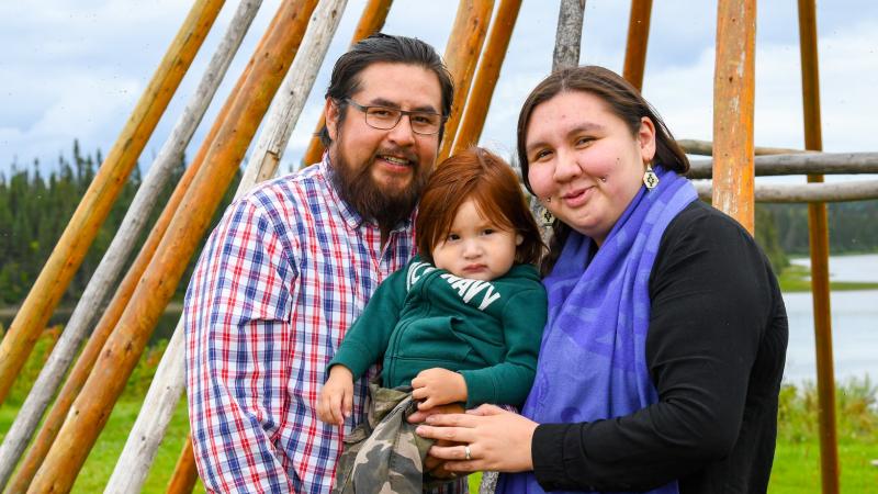 Father and mother holding child in front of teepee frame