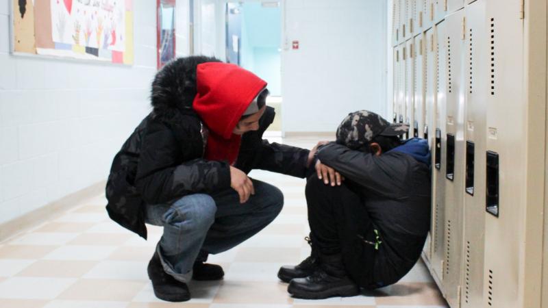 Youth helping another youth in a school hallway