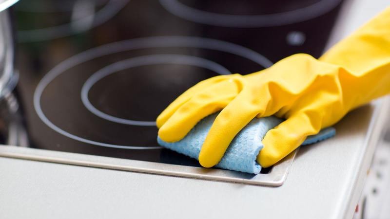Hand in yellow glove cleaning stovetop