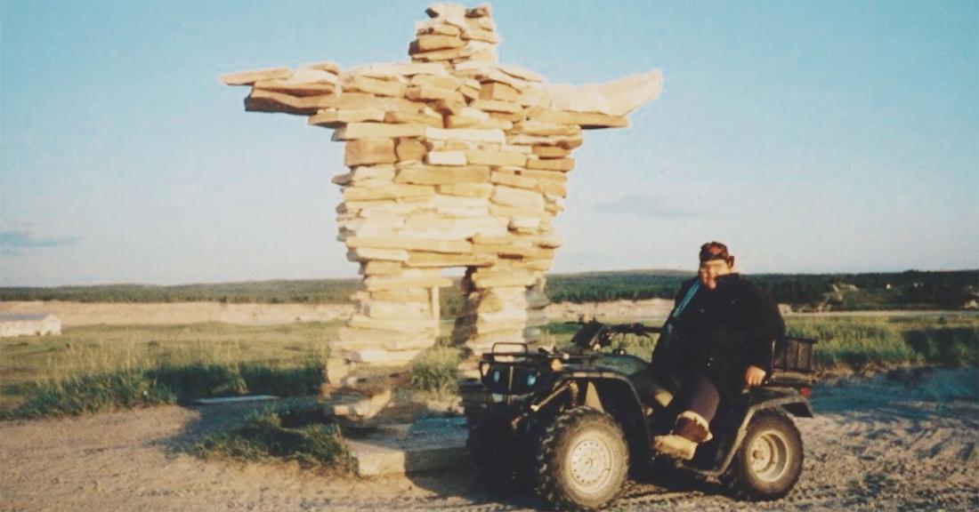 Buckley George riding ATV with Inukshuk in background