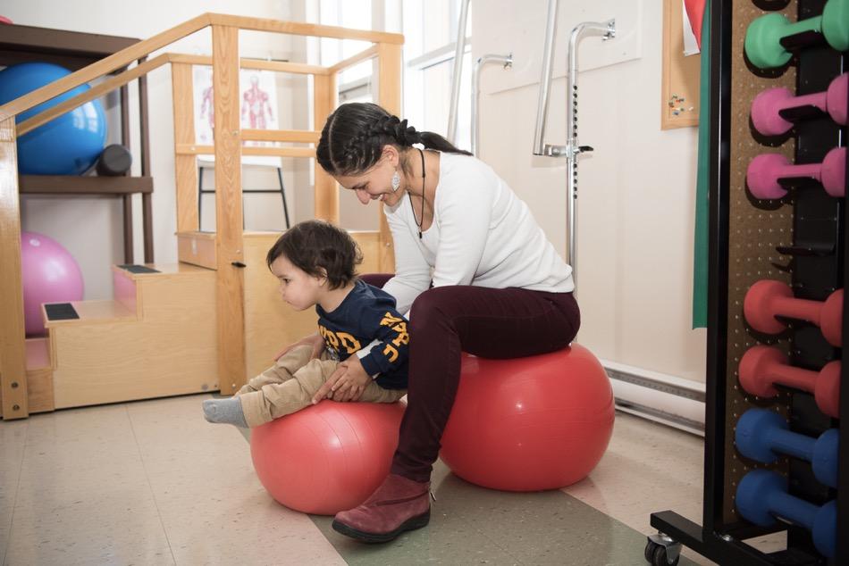 Woman sitting on inflatable ball helping a child balance on inflatable ball