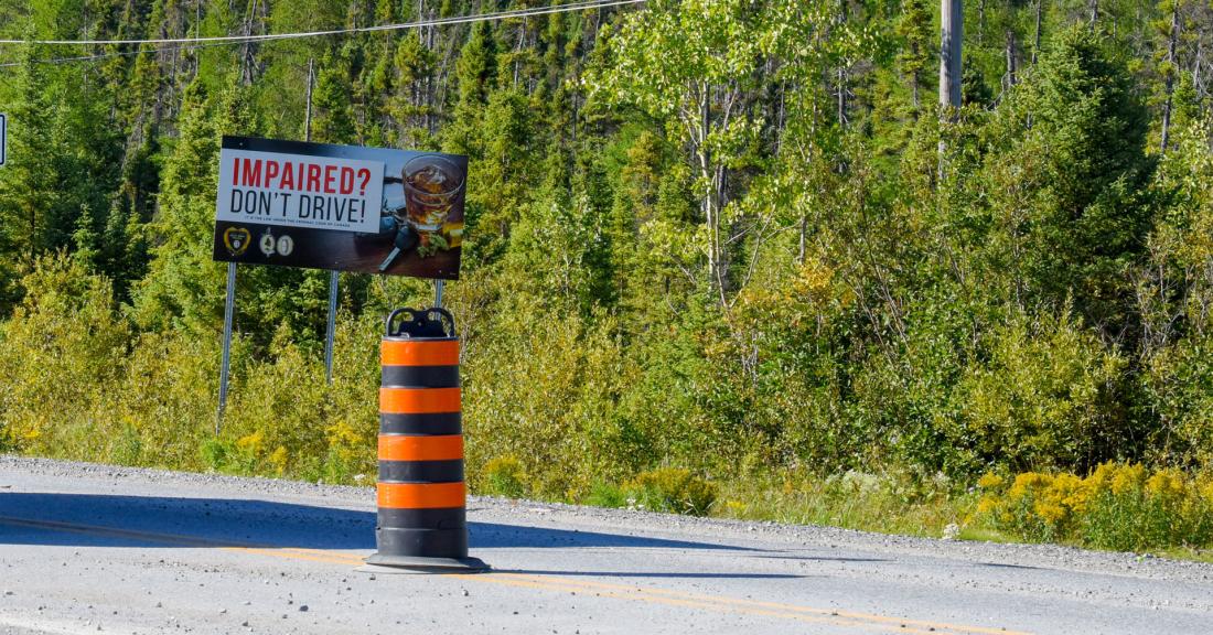 Orange pylon on road with Don't Drive Impaired sign