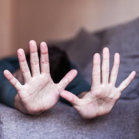 2 hands saying No with person lying on couch in background